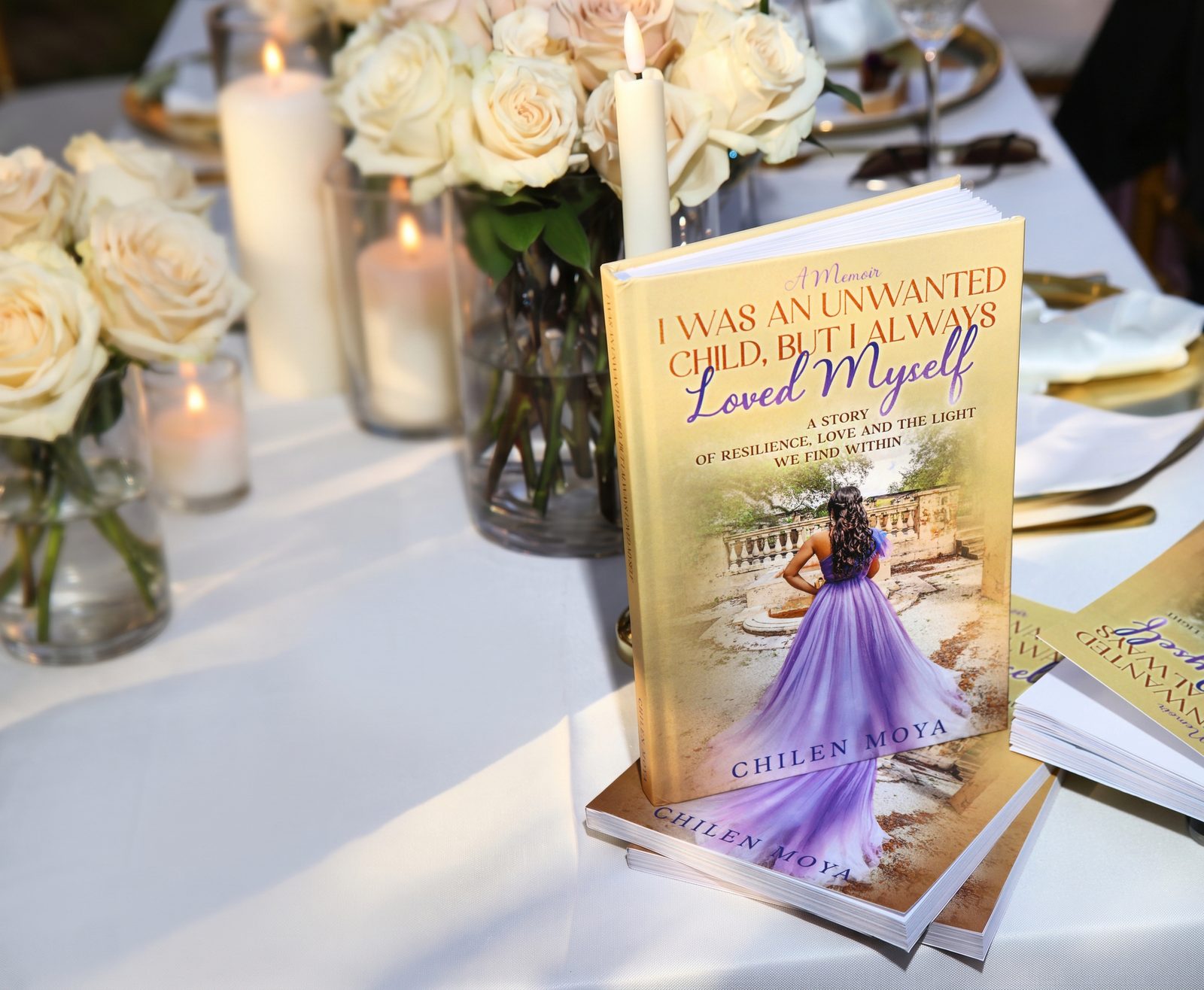 The memoir standing on a stack of copies on a candlelit table with ivory roses at the Miami rooftop book launch